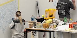Erwachsener zeigt einem Lehrling mit Pinsel Tricks fürs Malen
